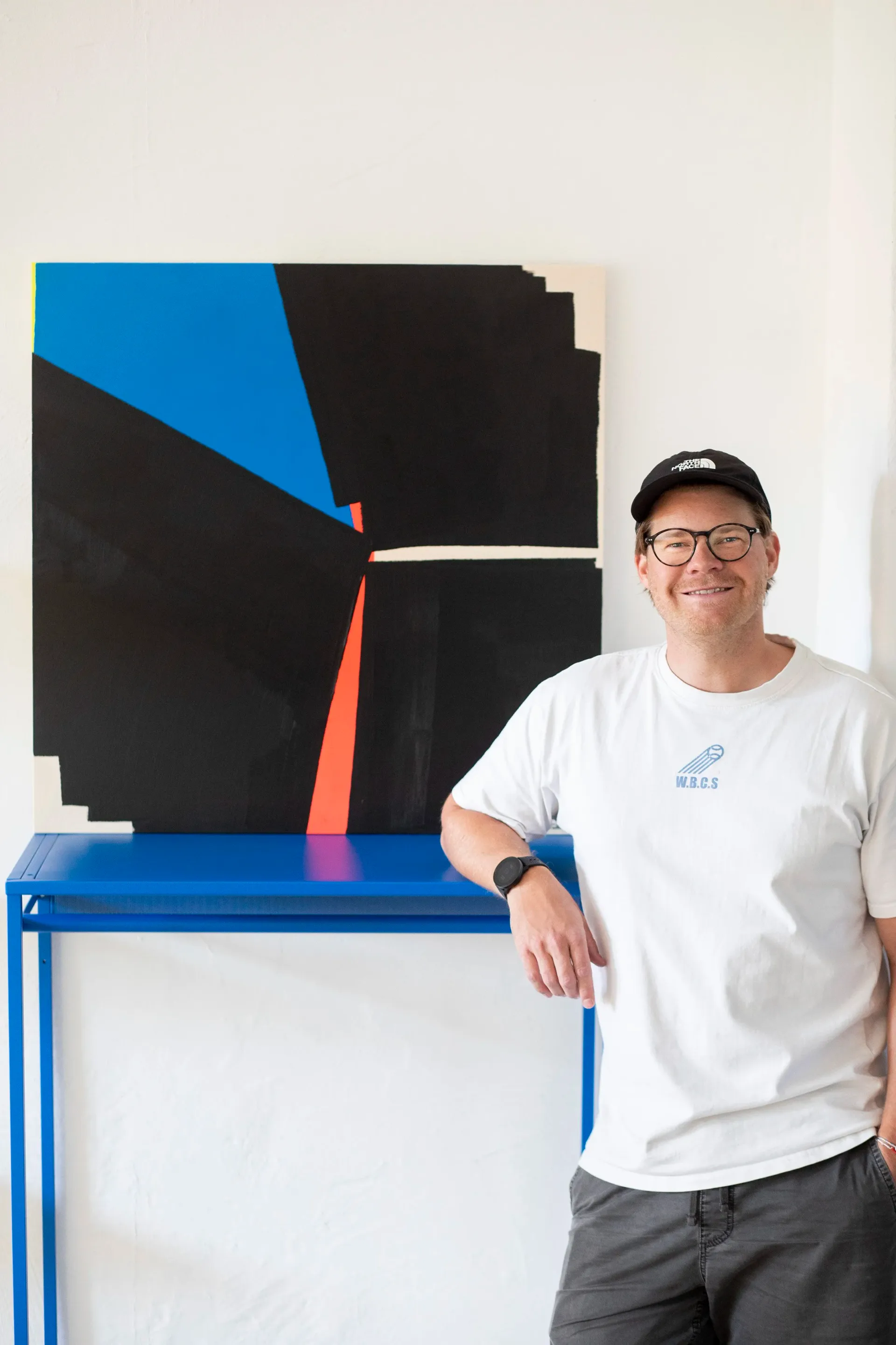 Dennis Fiedler neben einem seiner abstrakten, minimalistischen Kunstwerke in Schwarz, Kobalt und Neonrot