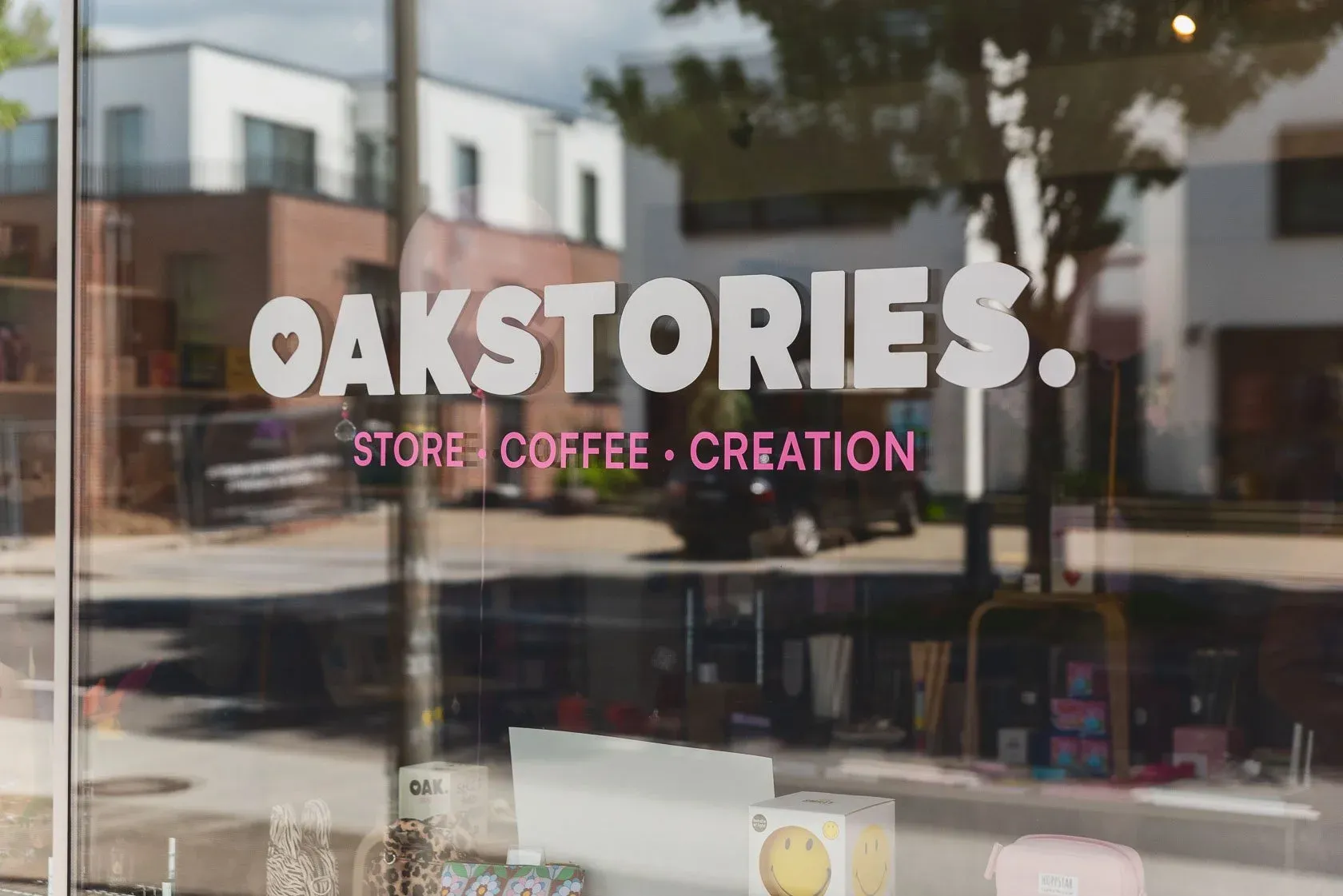 Das Schaufenster von oakstories. mit dem Logo auf der Scheibe und der Straße von Kirchhörde, die sich darin spiegelt